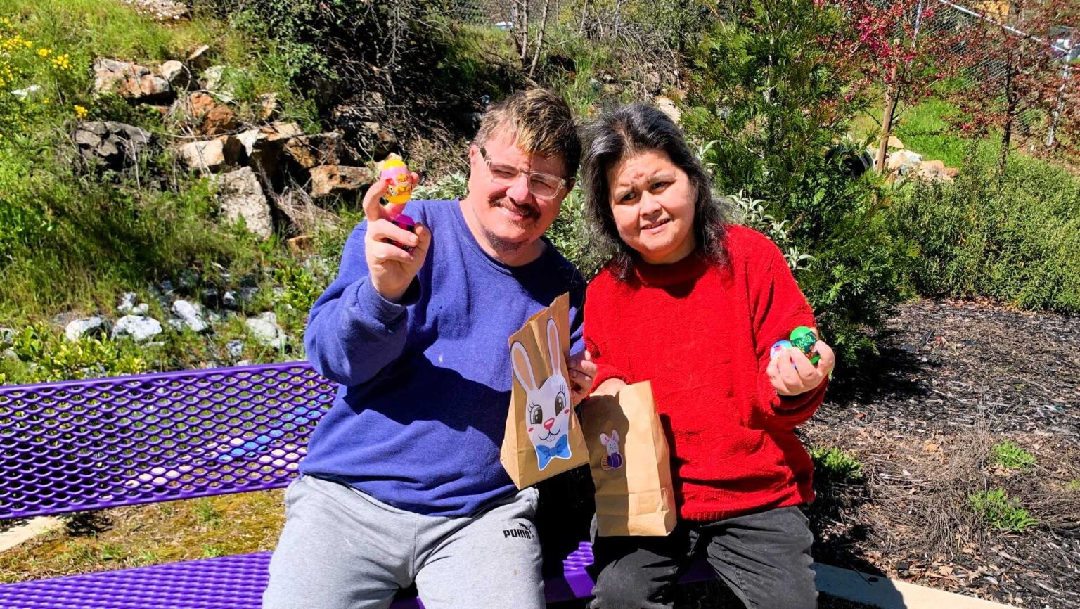 Two people sitting outside on a purple bench with Easter Egg treats